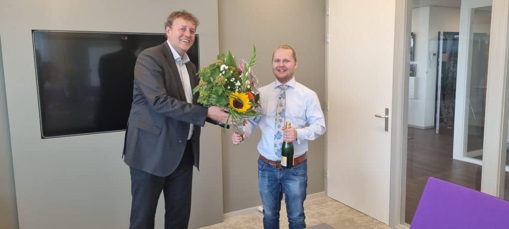 Edwin Koose overhandigd bos bloemen en fles champagne na ondertekening contract.