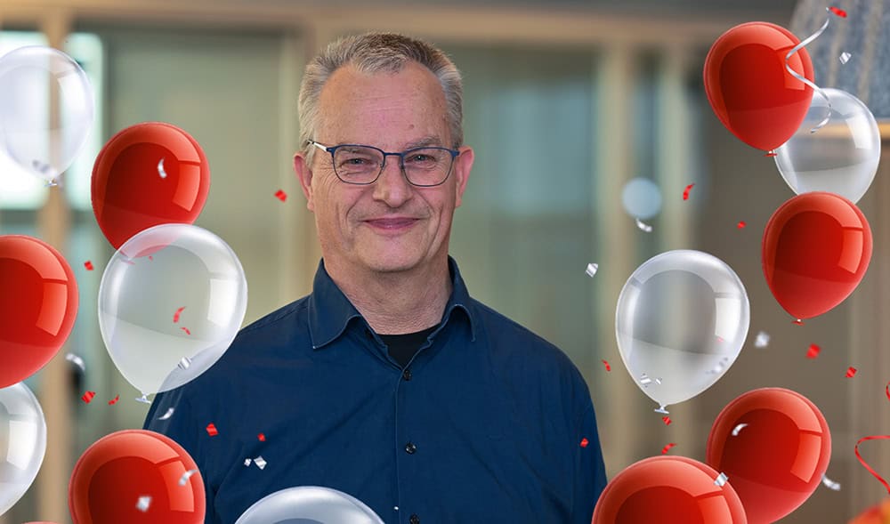 Smiling man in a blue shirt surrounded by red and white balloons and confetti.