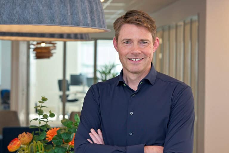 Robert Westdijk - Ventus Smiling man in a navy button-down shirt with arms crossed in a modern office setting.